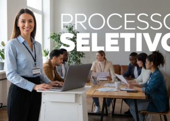 Imagem de uma profissional de pé em frente a uma mesa com outros colegas, representando um processo seletivo.