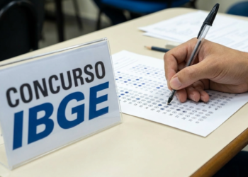 Pessoa preenchendo gabarito de concurso do IBGE, com placa visível ao fundo.