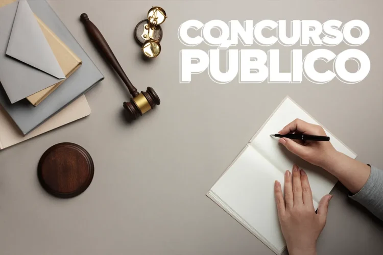 SAIU! Concurso do TJ-RS abre mais de 200 vagas para Cartórios 1 Mãos escrevendo em caderno próximo a martelo de juiz, bússola e envelopes sobre mesa.