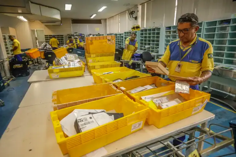 Concurso dos Correios é prorrogado: validade agora vai até 2027 2 Funcionários dos Correios organizando pacotes no centro de distribuição, com destaque para os processos logísticos.