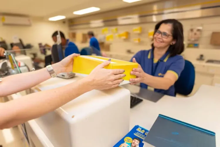 Concurso dos Correios é prorrogado: validade agora vai até 2027 1 Funcionária dos Correios entregando um pacote a um cliente, com destaque para o serviço postal.