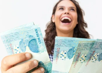 Mulher ri de felicidade enquanto exibe várias cédulas de R$ 100 com a mão estendida