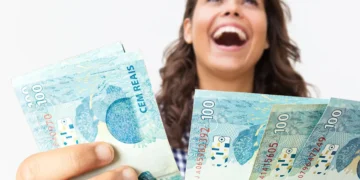 Mulher ri de felicidade enquanto exibe várias cédulas de R$ 100 com a mão estendida