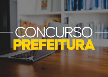 Notebook aberto sobre uma mesa de madeira em uma biblioteca, com o texto sobreposto "CONCURSO PREFEITURA" em destaque nas cores branco e amarelo.
