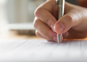 Mão segura caneta metálica e preenche formulário de inscrição em concurso público