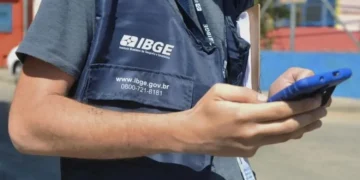 Agente do IBGE utilizando celular durante coleta de dados em campo, ilustrando expectativa para o novo concurso do instituto com 39 mil vagas previstas.