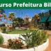 Jardim com flores e árvores ao centro de praça próxima a comércios em Bilac-SP, sob faixa do concurso