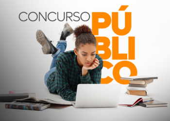 Jovem deitada usando notebook cercada de livros estudando para concurso público