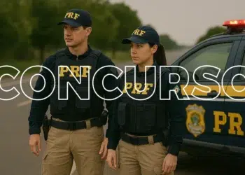 Dois agentes da Polícia Rodoviária Federal uniformizados posicionados ao lado de viatura oficial da PRF