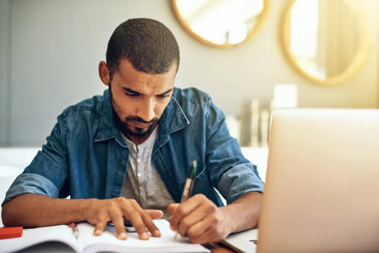Concurso público em 2026: nunca houve tantos motivos para deixar a CLT de lado (veja quais são eles) 1 Homem estudando para concurso público em 2026 enquanto analisa material de estudo ao lado do notebook.