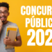 Rapaz sorridente com óculos segura cadernos e pastas, fundo amarelo com texto “Concursos Públicos 2026”