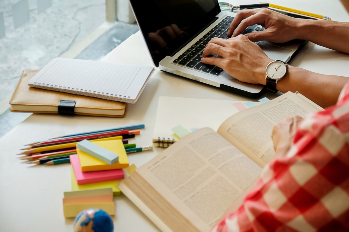 Quer se preparar para concursos antes do edital? Veja cinco dicas que fazem a diferença 2 Pessoa digitando em notebook enquanto consulta livro aberto e anotações coloridas