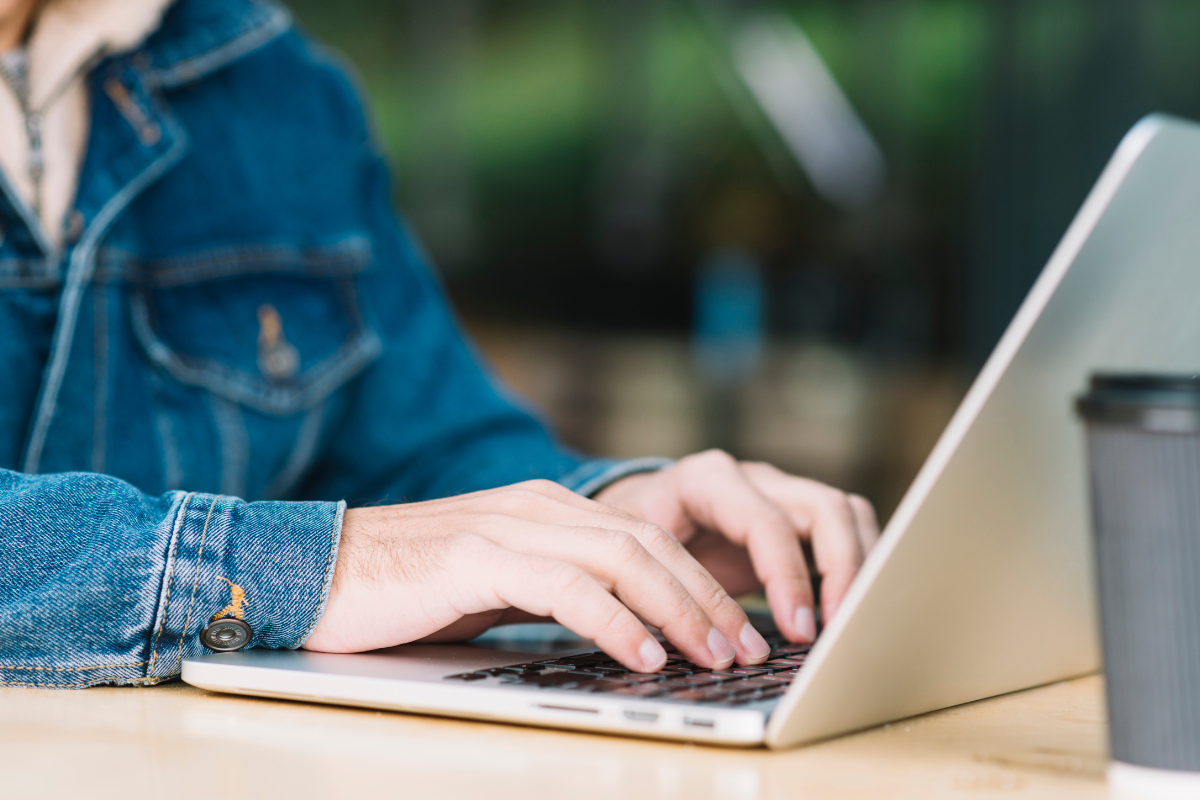 SAIU EDITAL! Concurso de Campos Novos Paulista com 12 vagas e salários de até R$ 4,4 mil encerra inscrições nos próximos dias 2 Pessoa com jaqueta jeans digitando em notebook ao lado de copo descartável