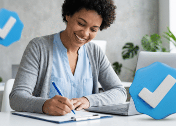 Mulher sorrindo escreve em caderno ao lado de notebook e selos de verificação azuis