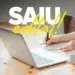 Pessoa escrevendo em caderno ao lado de notebook, caneca branca e texto “SAIU edital!” em destaque