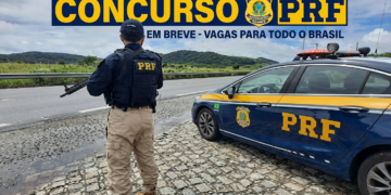 Policial rodoviário federal armado ao lado de viatura PRF em rodovia pavimentada com paisagem montanhosa