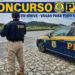 Policial rodoviário federal armado ao lado de viatura PRF em rodovia pavimentada com paisagem montanhosa