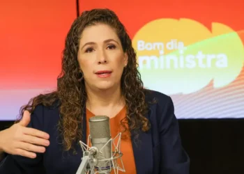 Esther Dweck fala ao microfone em estúdio com fundo colorido escrito "Bom dia, ministra"