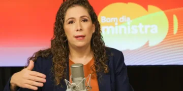 Esther Dweck fala ao microfone em estúdio com fundo colorido escrito "Bom dia, ministra"