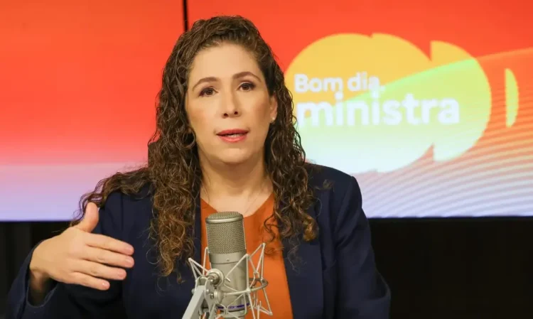 Esther Dweck fala ao microfone em estúdio com fundo colorido escrito "Bom dia, ministra"