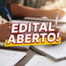Processo seletivo no IFRS: vaga para Professor de Ciências Biológicas com remuneração de até R$ 14.124,01 9 Estudantes escrevem em cadernos sobre mesa de madeira com destaque para letreiro "Edital Aberto!" em vermelho e amarelo.