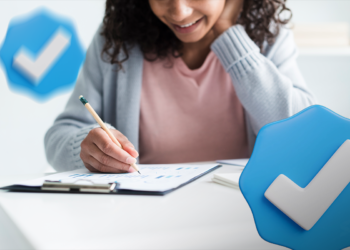Mulher de cabelos cacheados escreve em gráficos sobre mesa branca ao lado de ícones de selo azul de verificação